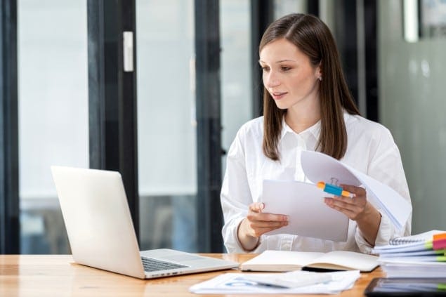 mulher trabalhando em notebook com documento físico em mãos
