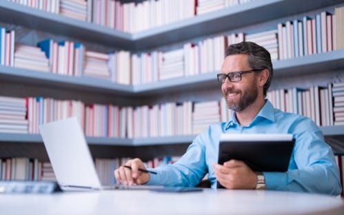 professor trabalhando em um notebook dentro da biblioteca